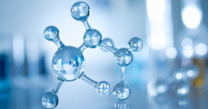 A close-up of a shiny, silver molecular model with connected spheres representing atoms, set against a blurred blue and white laboratory background.