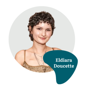 A person with short curly dark hair smiling, wearing a tan patterned top and layered necklaces. Text on a blue shape reads: “Eldiara Doucette.” The background is light gray with a white circular frame.